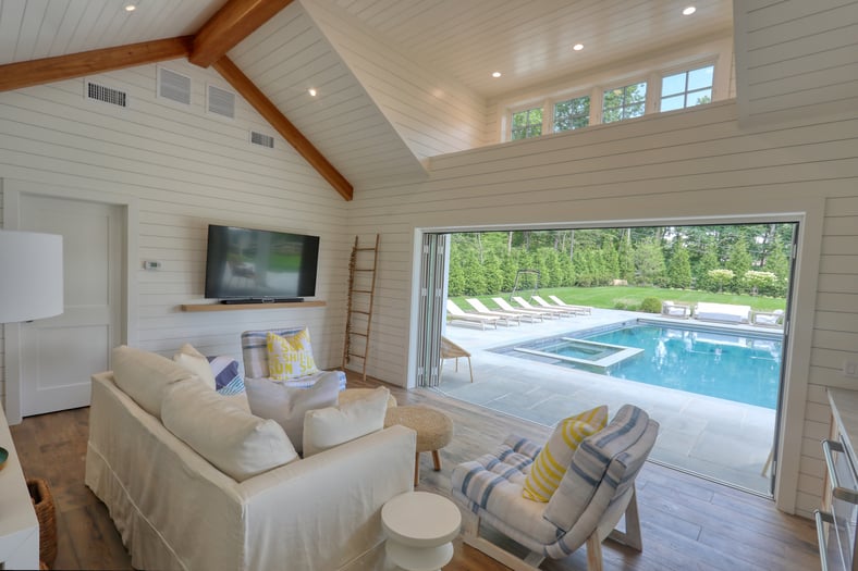 interior shot of pool house facing pool, with couch and chairs, by Raymond Design Builders in Fairfield County, CT