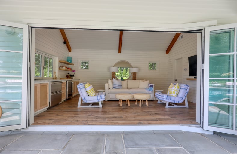 pool house with doors open, chairs, and couch, by Raymond Design Builders in Fairfield County, CT.