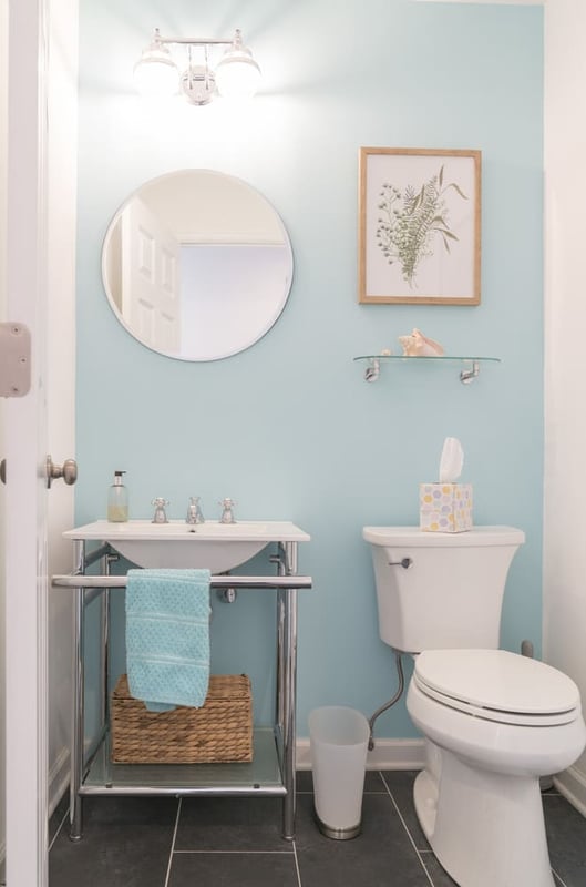 blue walls powder room with toilet and round gold trimmed mirror above small sink by raymond design builders