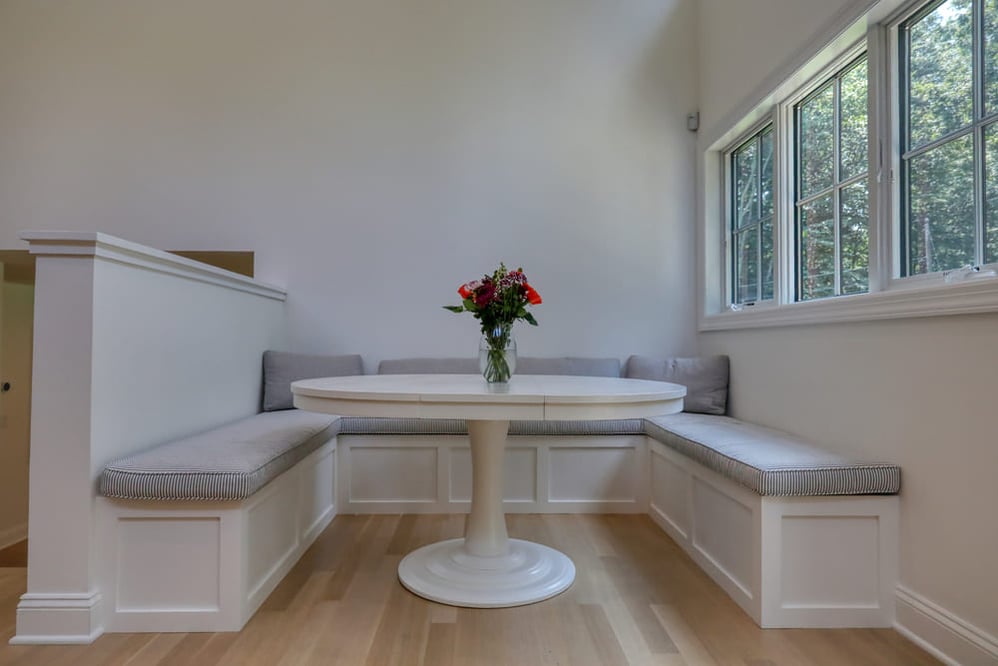 white breakfast nook in kitchen with gray cushions in booth and large windows by raymond design builders in ct