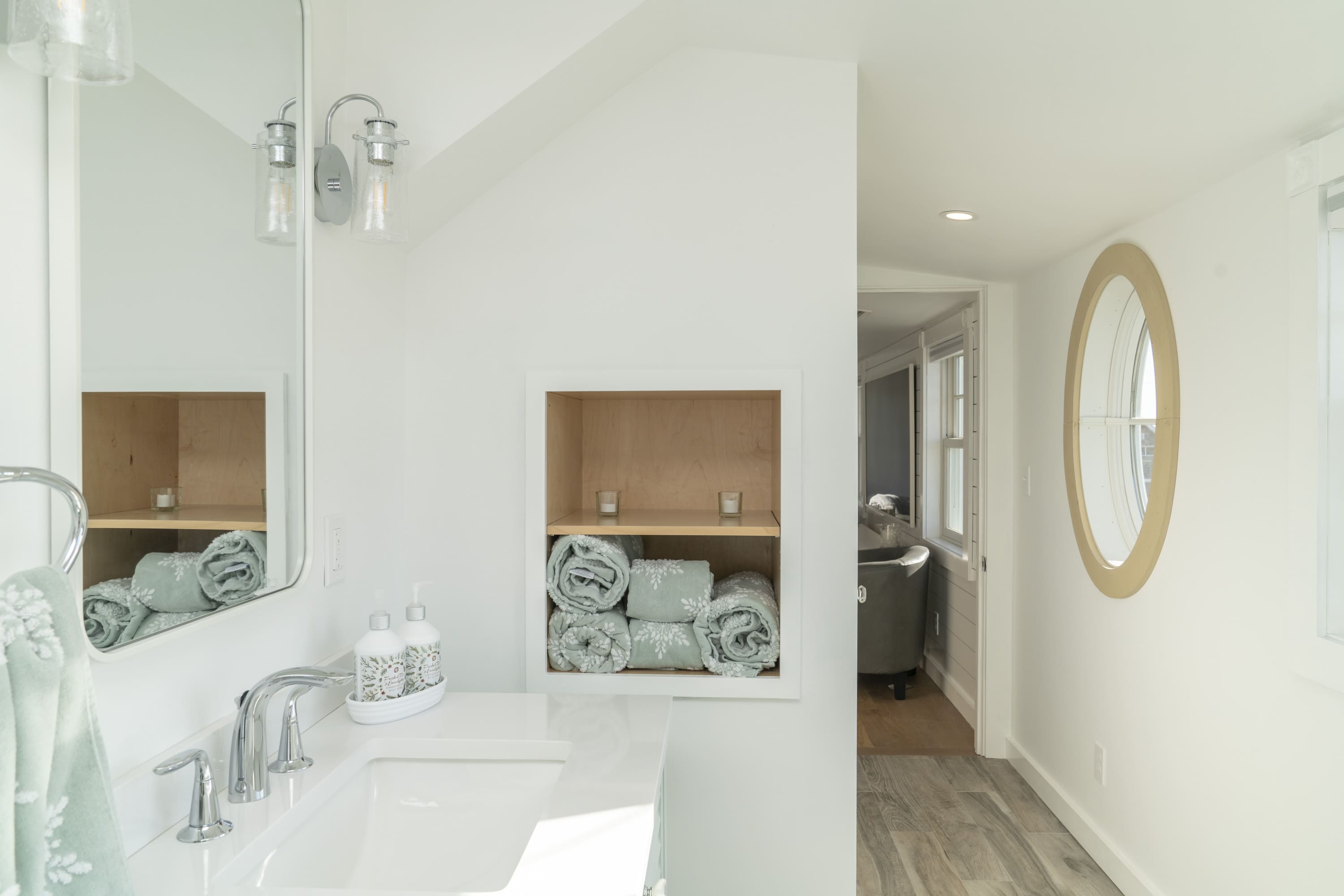 white bathroom with green accents and beige round window by raymond design builders