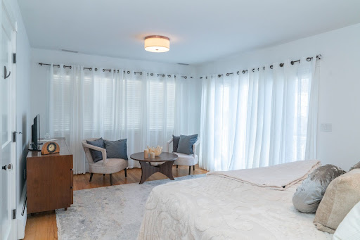 white bedroom with grey chairs and round table at end of bed by raymond design builders