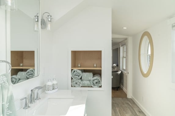 white bathroom with green accents and beige round window by Raymond Design Builders