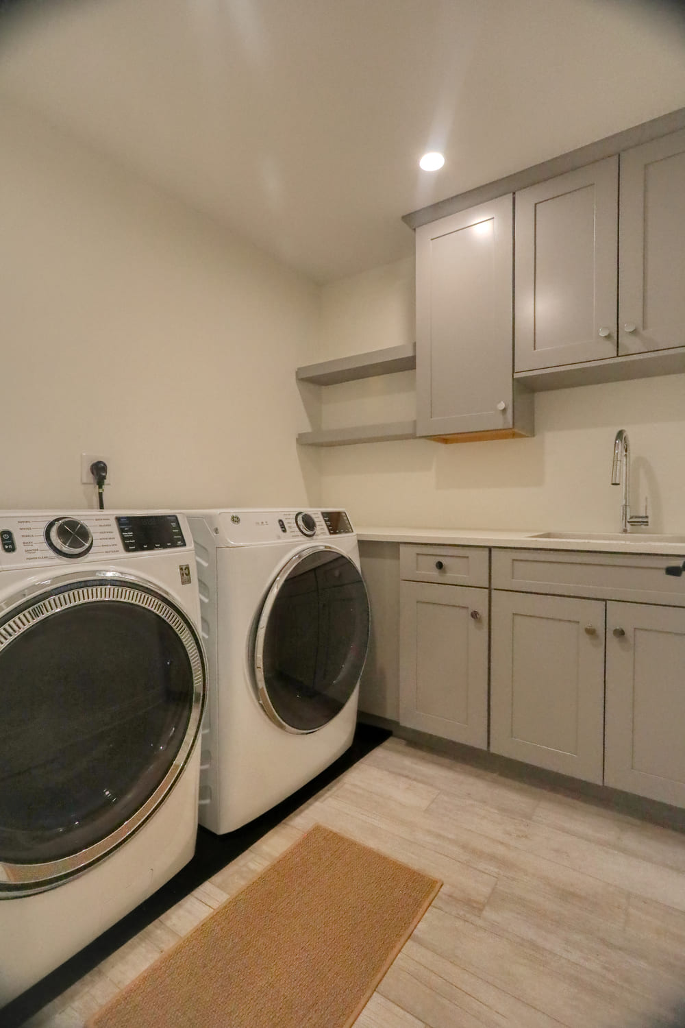 modern white laundry room with grey cabinetry and hardwood flooring by raymond design builders in ct