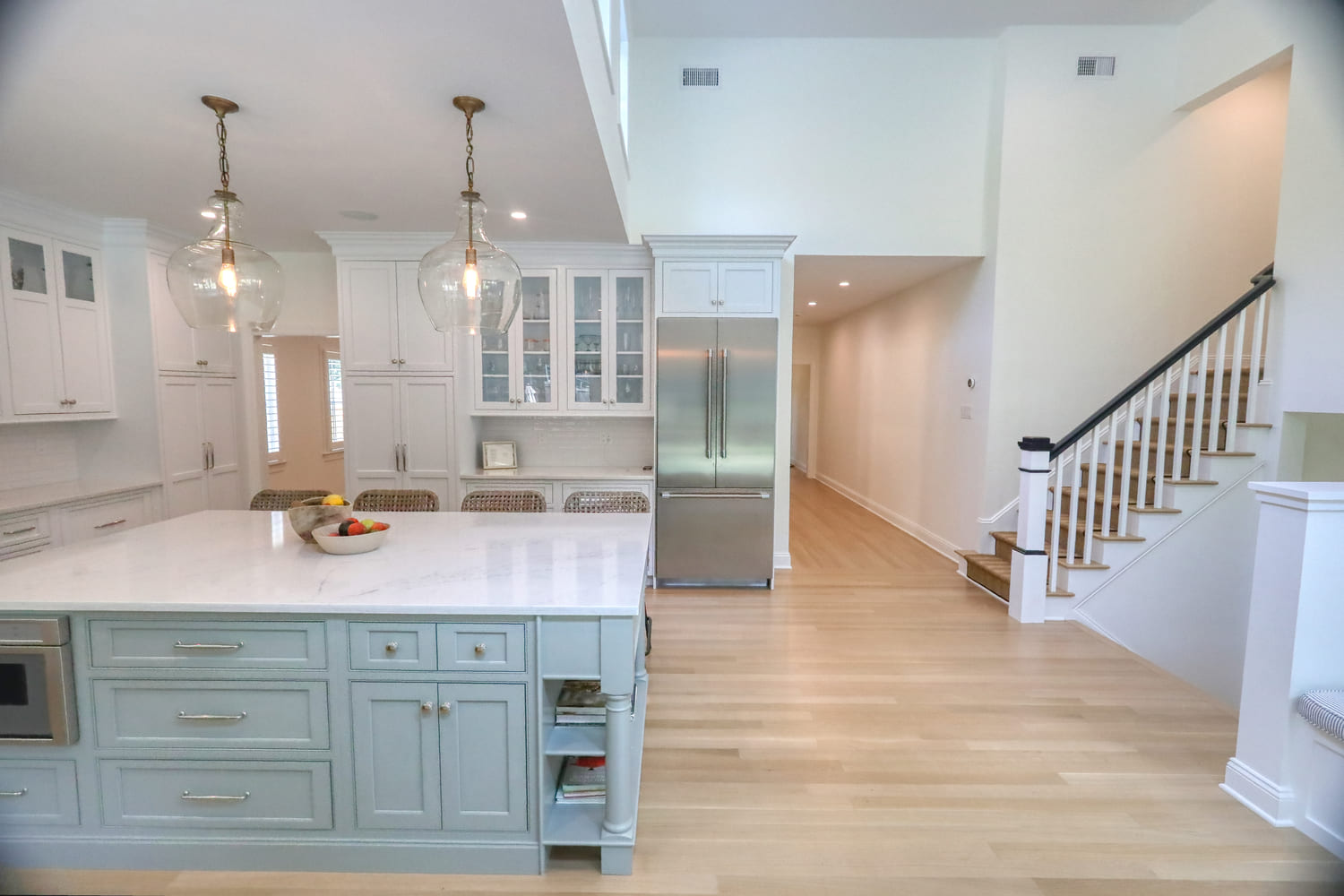 white modern farmhouse kitchen with large island and wicker bar stools by raymond design builders in westport